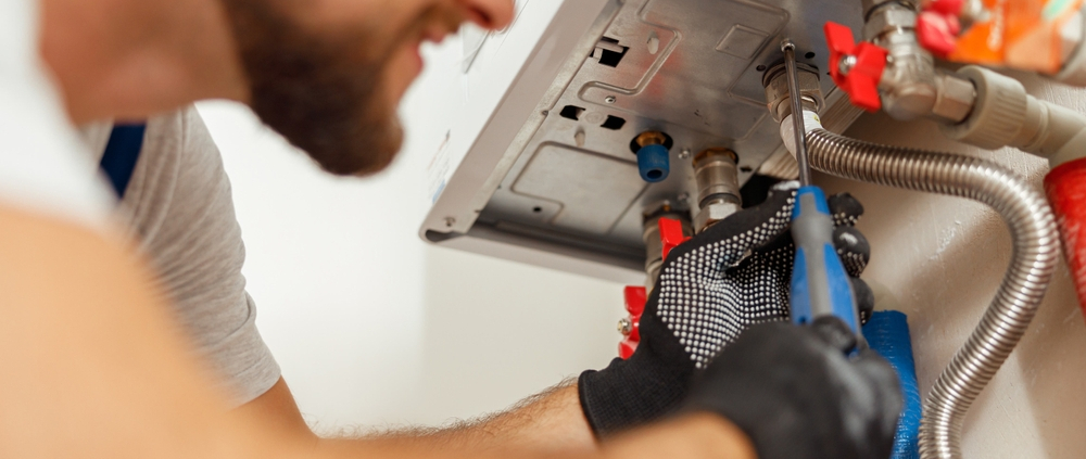 Closeup of plumber using screwdriver while installing new steel hot water central heating system in apartmen