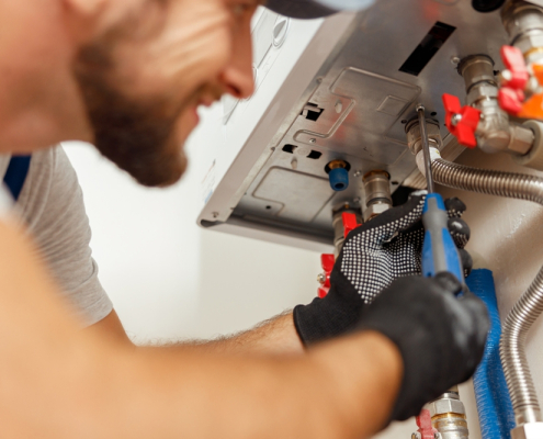 Closeup of plumber using screwdriver while installing new steel hot water central heating system in apartmen