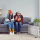 Freezing people in winter jackets sitting on sofa at home. Sad warmly closed husband abd wife feeling cold and trying to warm up. Heating problems, power crisis concept